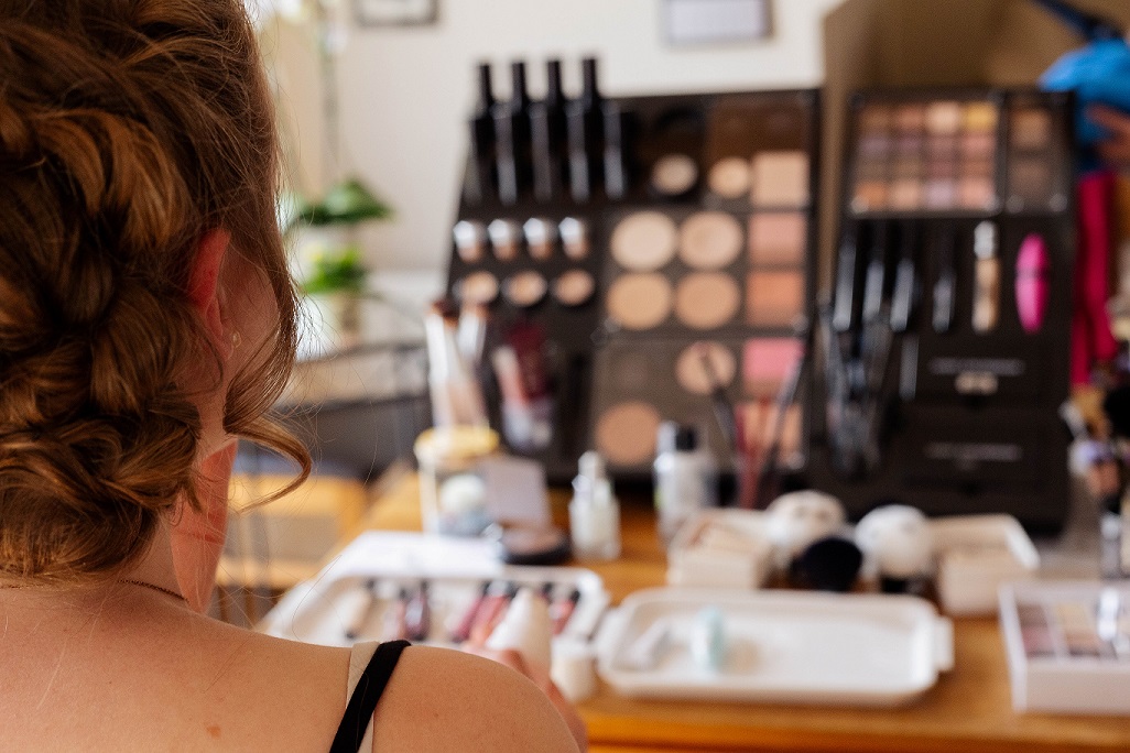 Braut sitzt w&auml;hrend des Make-up-Coachings vor einem Tisch mit vielen Schminkutensilien