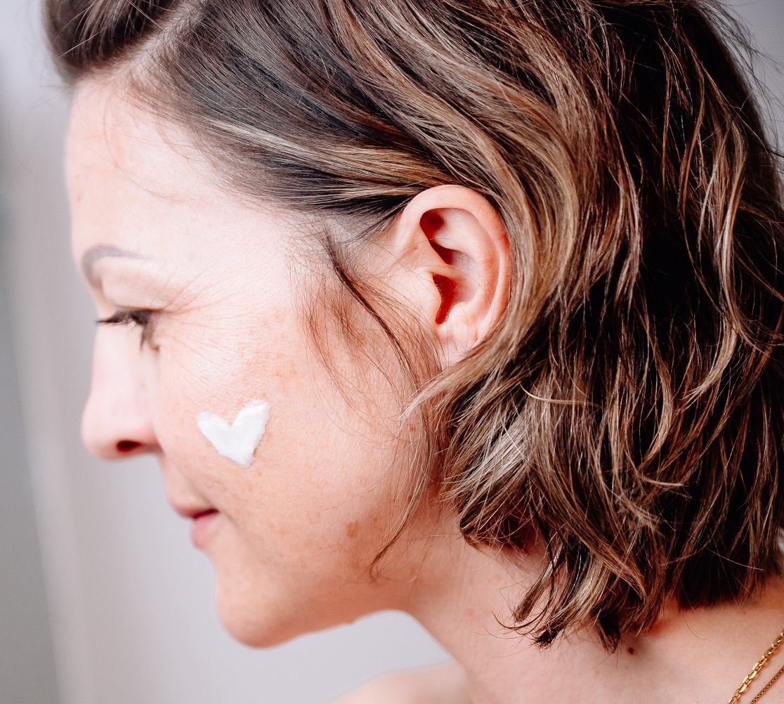 Frau hat ein Herz aus Creme im Gesicht